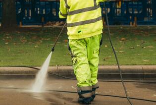 a city worker in high visibility gear pressure washing a street corner